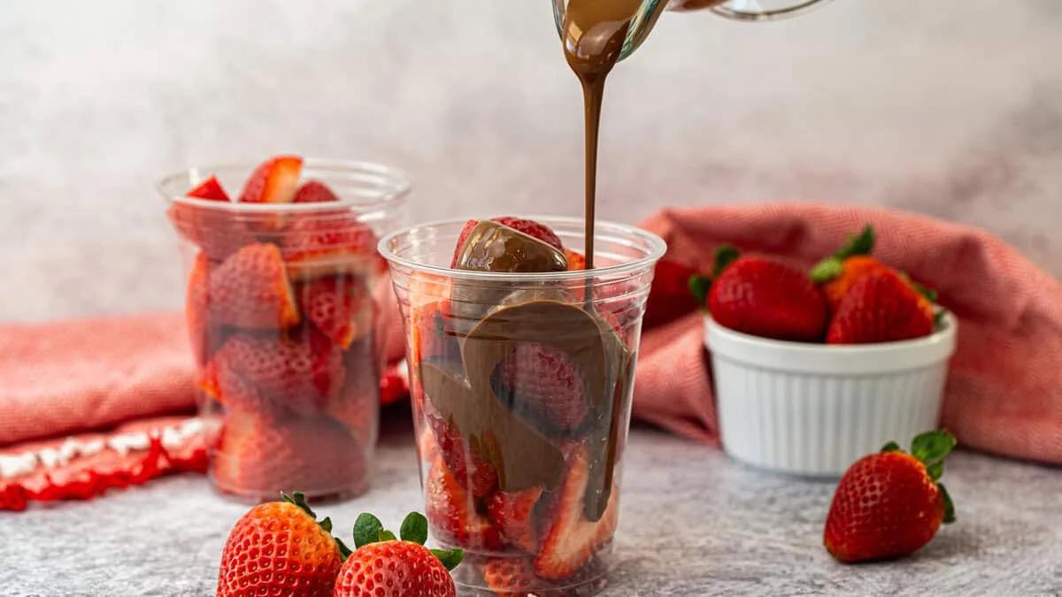 Chocolate being poured over fresh strawberries in a cup
